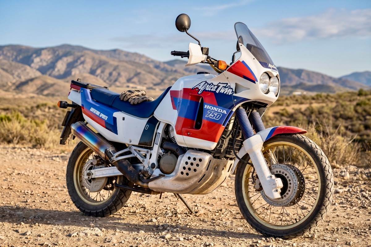 Honda Africa Twin 750 motorcycle in white, red and blue livery parked on a desert dirt road with mountains.